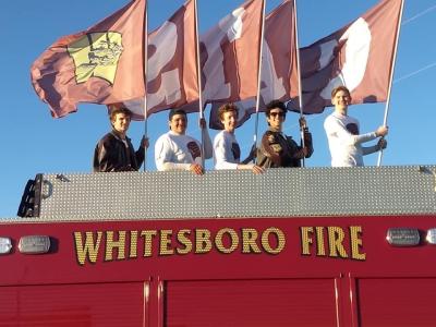 School students standing on top of fire truck holding flags